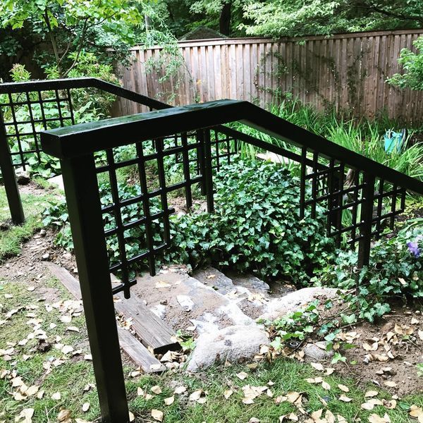 A set of outdoor stone steps descending into a garden, flanked by dark brown wooden railings with a grid-patterned fence.