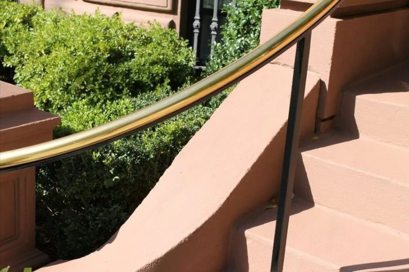 Curved pink staircase with black handrail beside green shrubs in sunlight