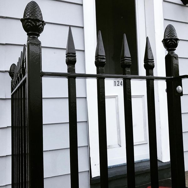 Black metal fence with decorative finials in front of a white house entrance marked 124.