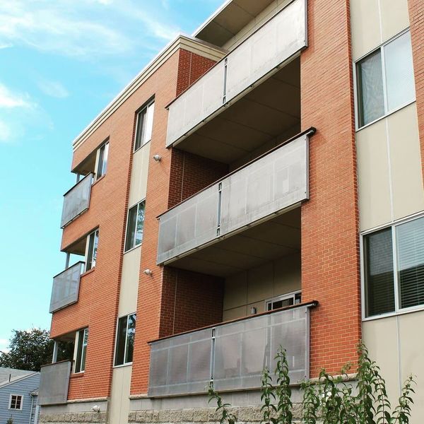 Modern multi-story apartment building with orange brick exterior, recessed balconies, and large windows against a blue sky.