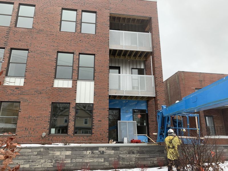Construction worker in a safety harness operating a blue lift near the brick exterior of a multi-story building.
