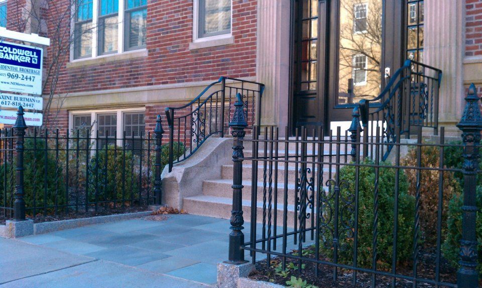 Brick townhouse entrance with black iron fence, steps, and sidewalk in front