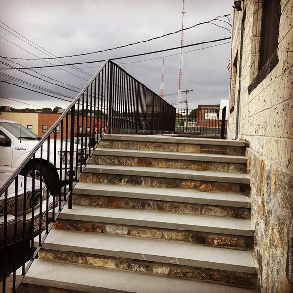 A stone staircase leading up to a building entrance with a black metal handrail alongside it.