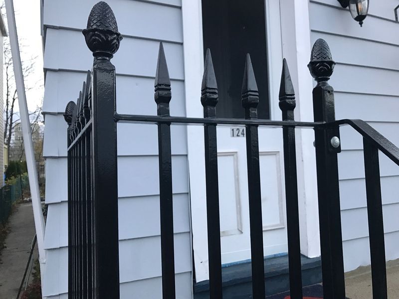 Black iron railing with pineapple finials and pointed pickets in front of a white house entrance.