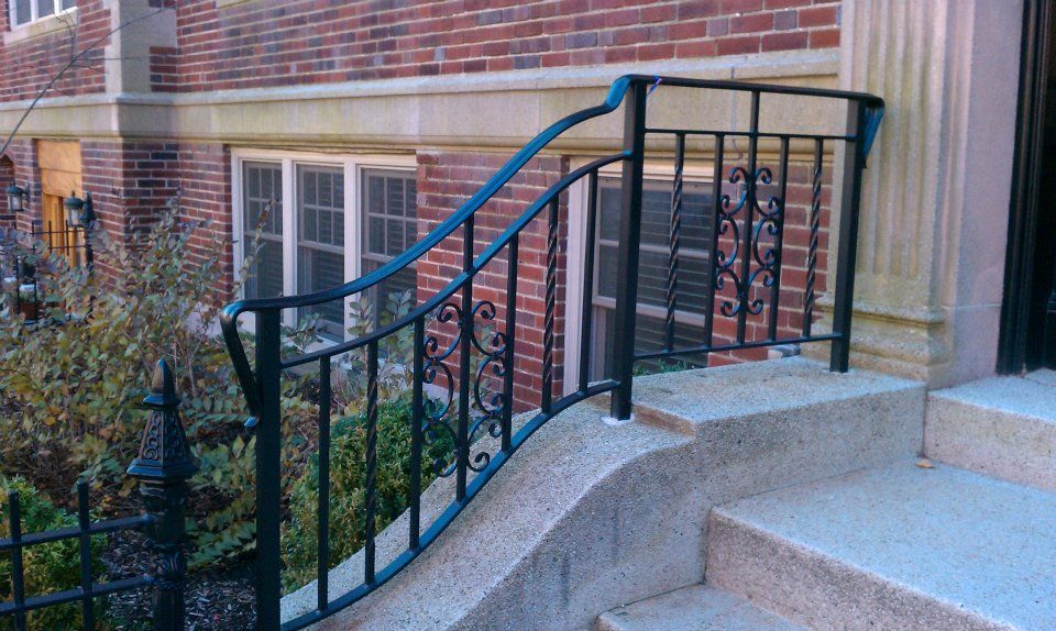 Black metal handrail on concrete steps beside a brick building entrance ramp