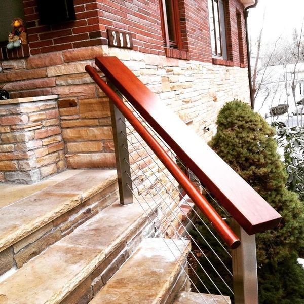 Modern stainless steel railing with a wooden handrail installed on stone steps leading up to a brick and stone house.