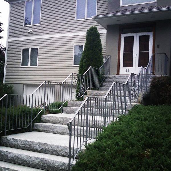 Wide stone stairs with metal railings leading to the front entrance of a two-story house with gray siding.