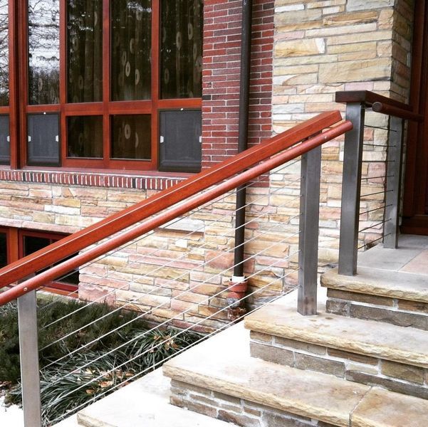 Stone steps with metal and wood handrails, horizontal cable railings, and a red brick and stone exterior wall.