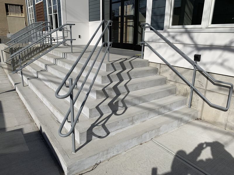 A set of concrete outdoor stairs with metal handrails leading to a building entrance.
