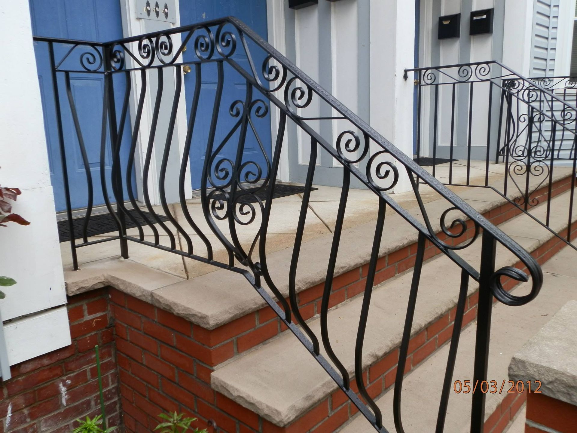 Decorative black wrought-iron stair railing on red brick steps outside a house