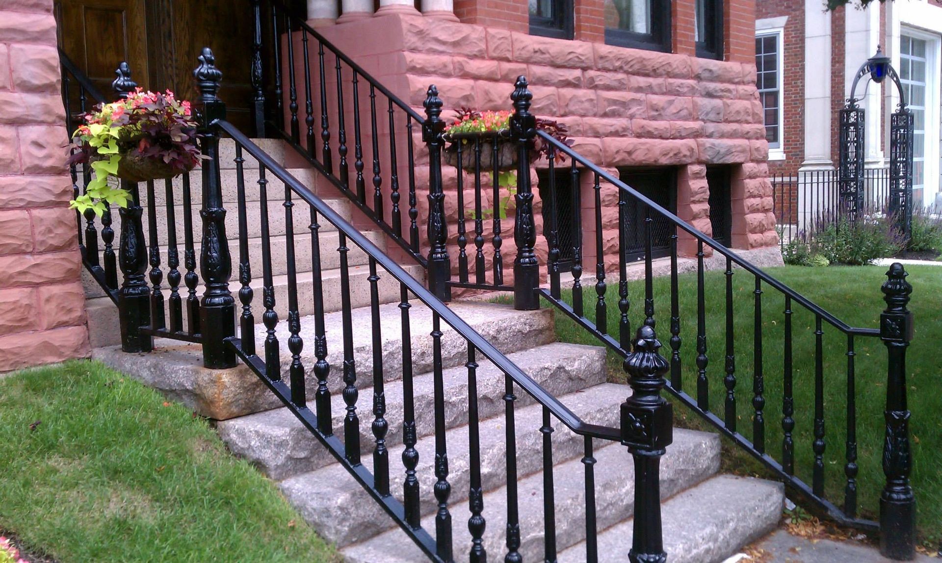 Stone steps with black railings leading to a pink brick house entrance, with flower planters nearby