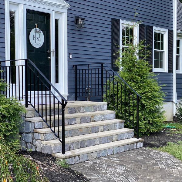 A set of stone steps leading to a dark blue house entrance with a black metal railing and a round welcome sign on the door.