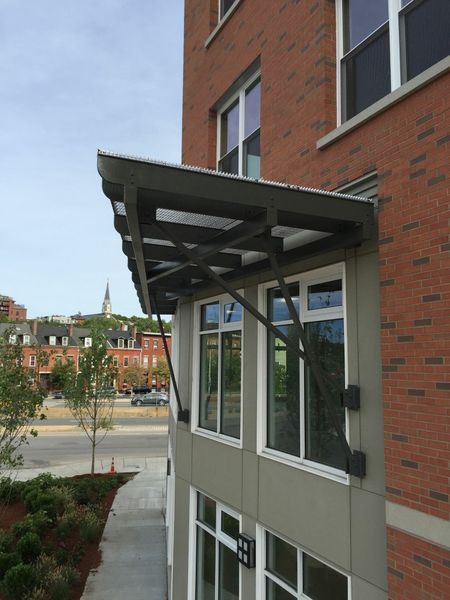 A modern metal awning projects over the first-floor windows of a red brick building.
