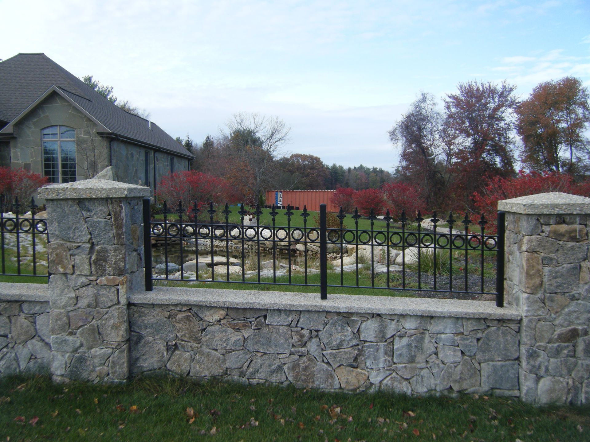 Stone fence and black metal gate in front of a house and landscaped garden