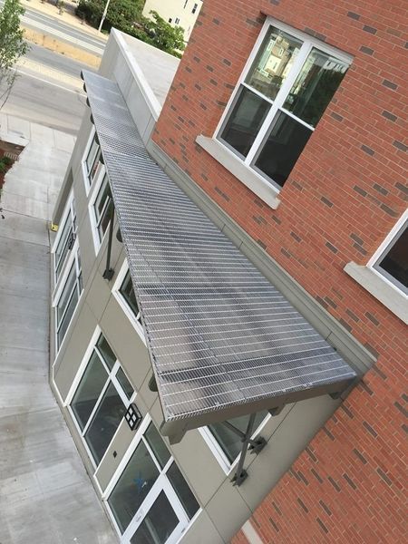 High-angle view of a grey metal slatted canopy attached to a brick building facade above a set of glass doors.