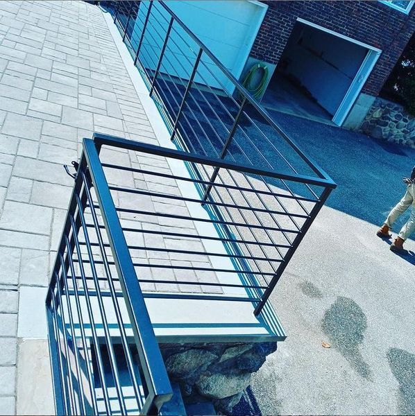 A black metal railing installed on a stone-based patio overlooking a driveway and garage entrance.