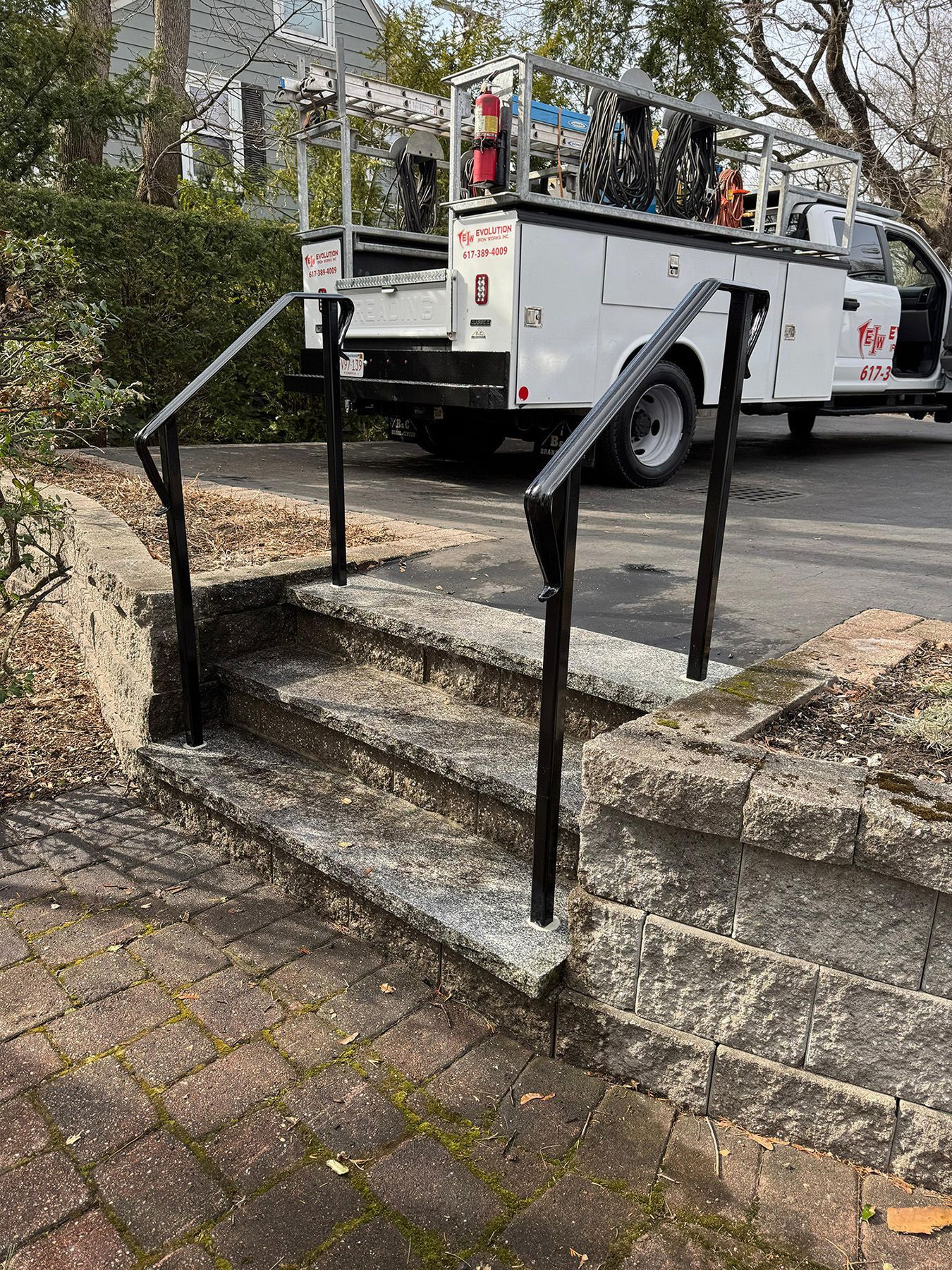 Stone steps with black railings leading to a white utility truck on a street