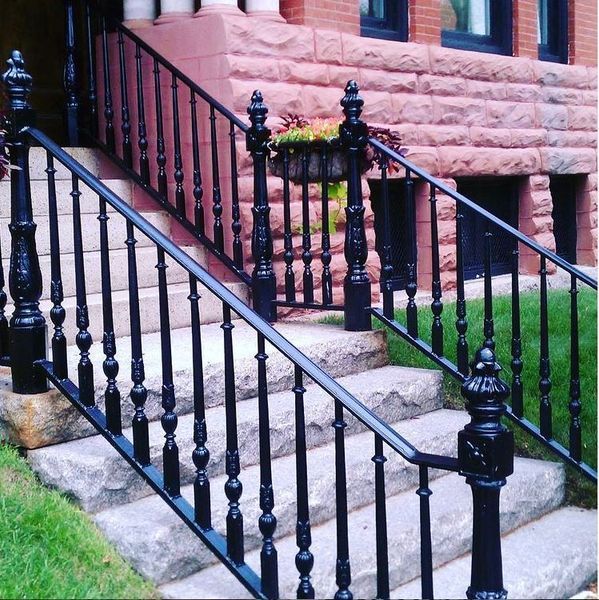 Black decorative iron railings line stone steps leading to a brick building entrance with a floral planter.
