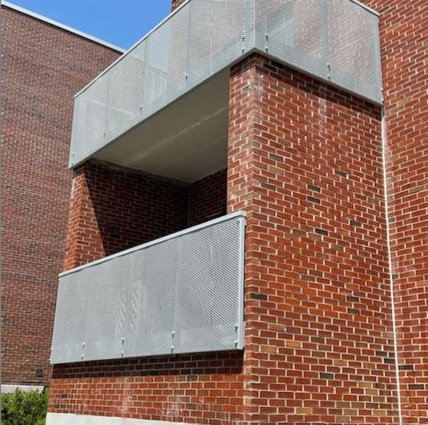 A red brick building with two stacked balconies featuring silver, perforated metal railings.