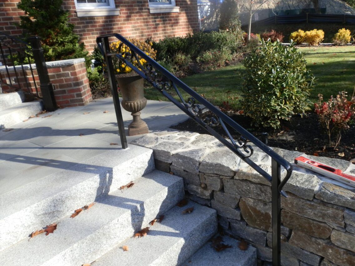 Stone steps with a black metal railing beside a brick house and garden.