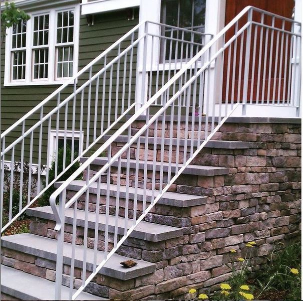 A stone staircase with white metal railings leading up to a house entrance with olive green siding and a wooden door.