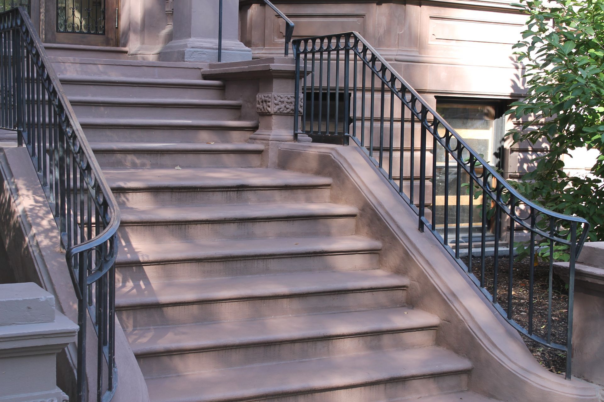 Front steps of a brownstone with black wrought-iron railings and a small staircase leading to the entrance.