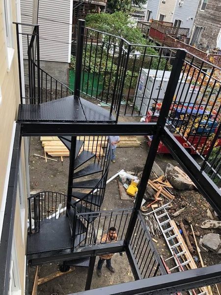 A black metal spiral staircase and balcony frame under construction outside a multi-story building.