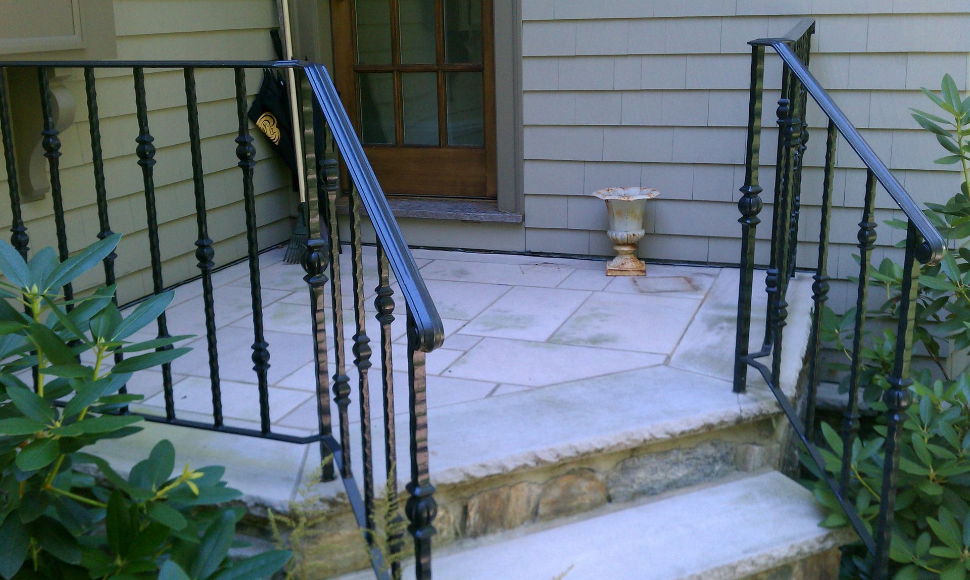 Front porch with black metal railings, light stone steps, and a white bench near the door