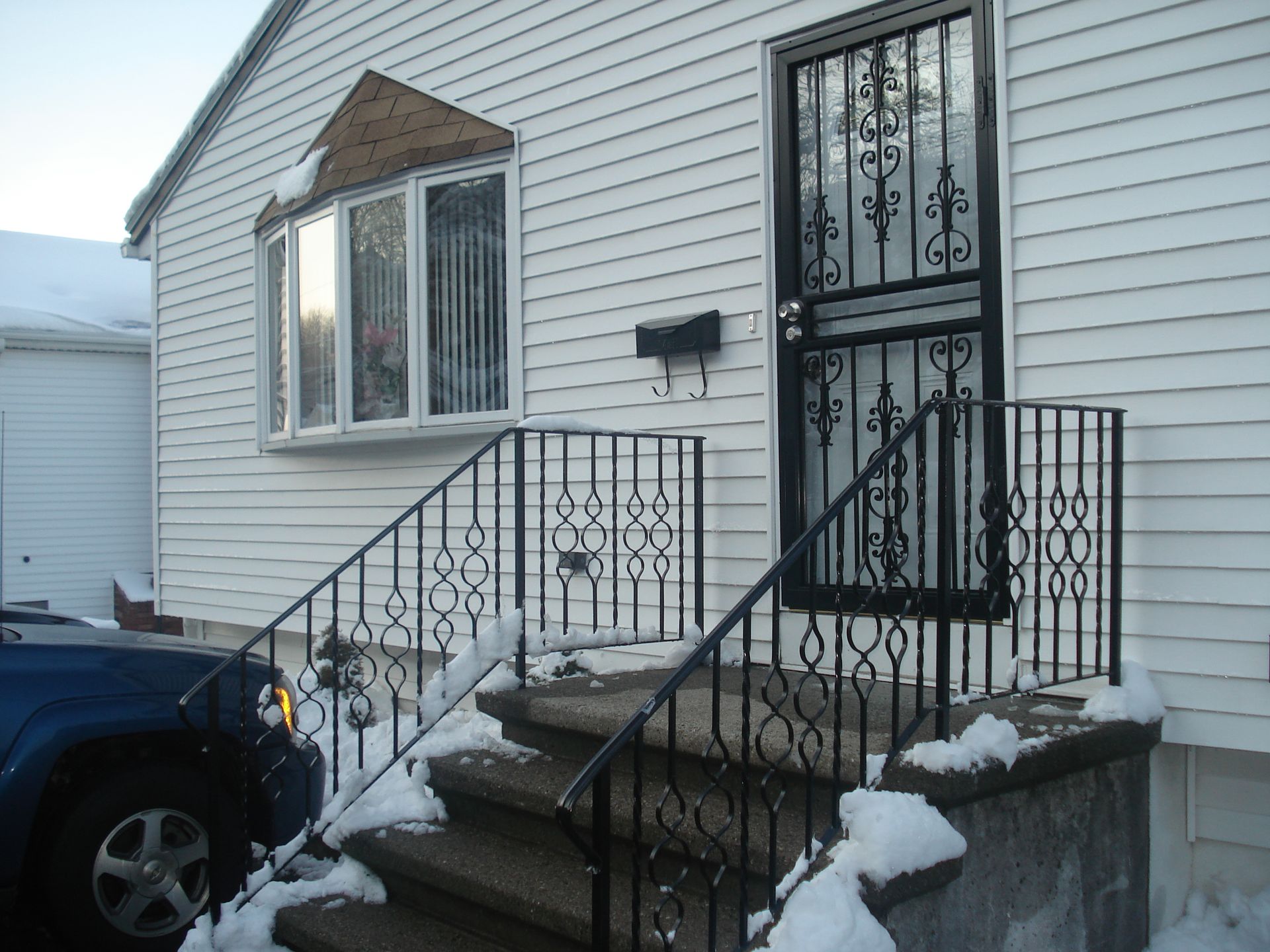 Snowy front steps leading to a white house with black railings and a parked car nearby