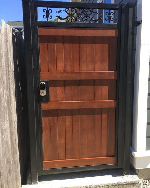 A wooden pedestrian gate with a black metal frame, decorative top scrollwork, and an electronic keypad lock.