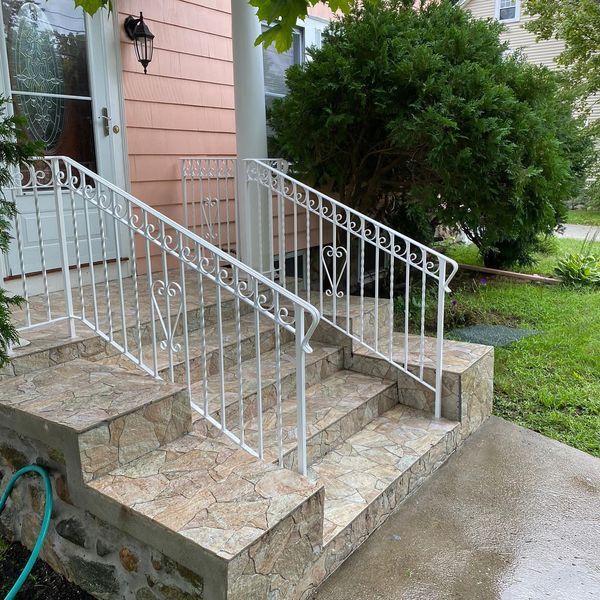 Front steps with stone-look tile, white metal railings, and decorative heart accents leading to a house entrance.