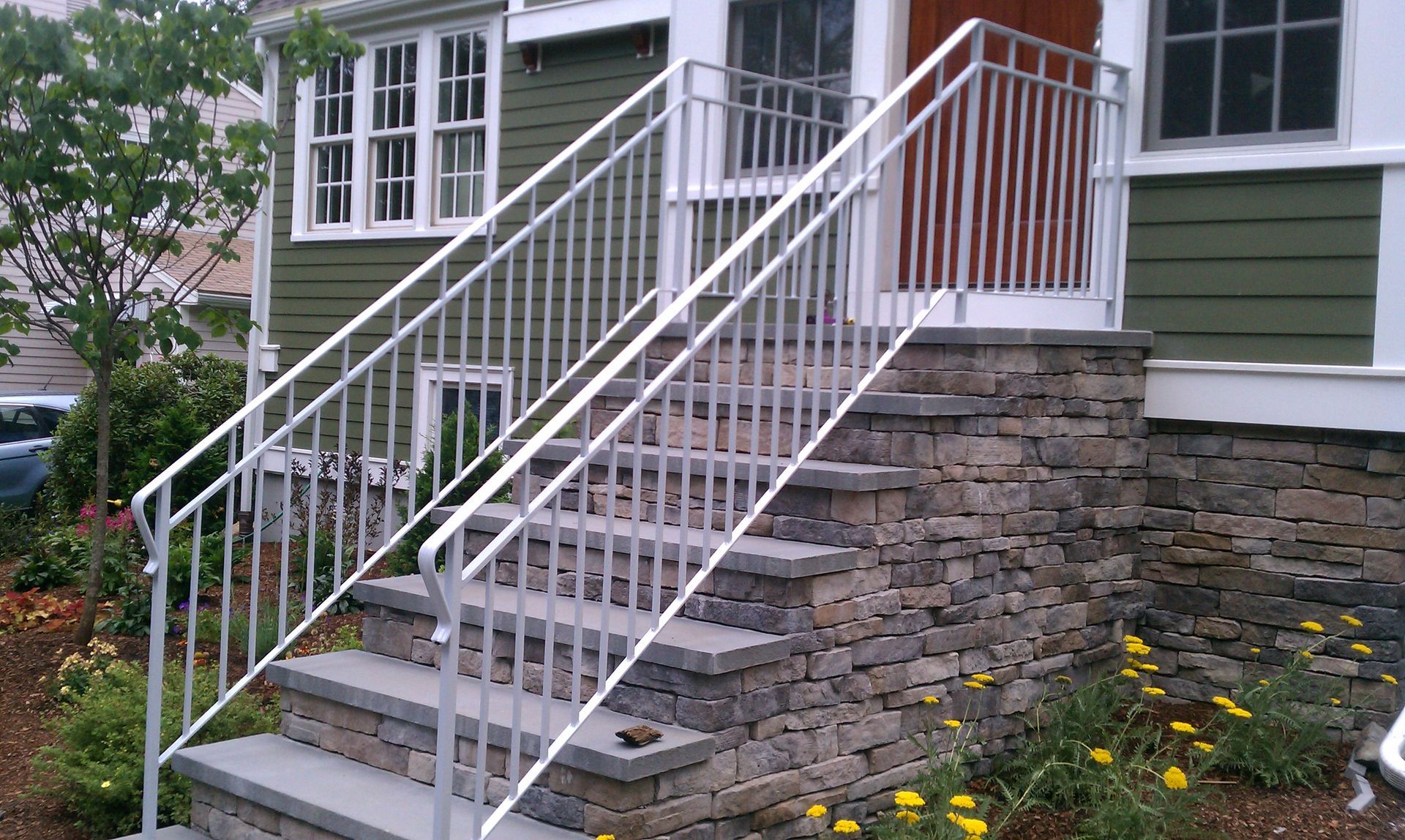 Stone front steps with white railings leading to a green house entrance