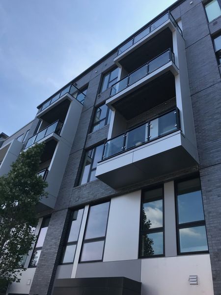 A low-angle view of a modern gray multi-story apartment building with stacked glass-railed balconies against a blue sky.