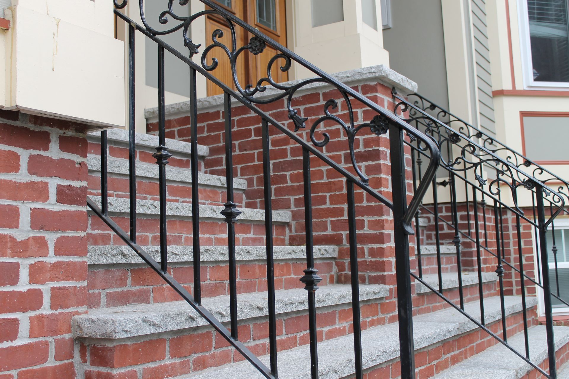 Red brick outdoor staircase with black wrought-iron railing beside a building