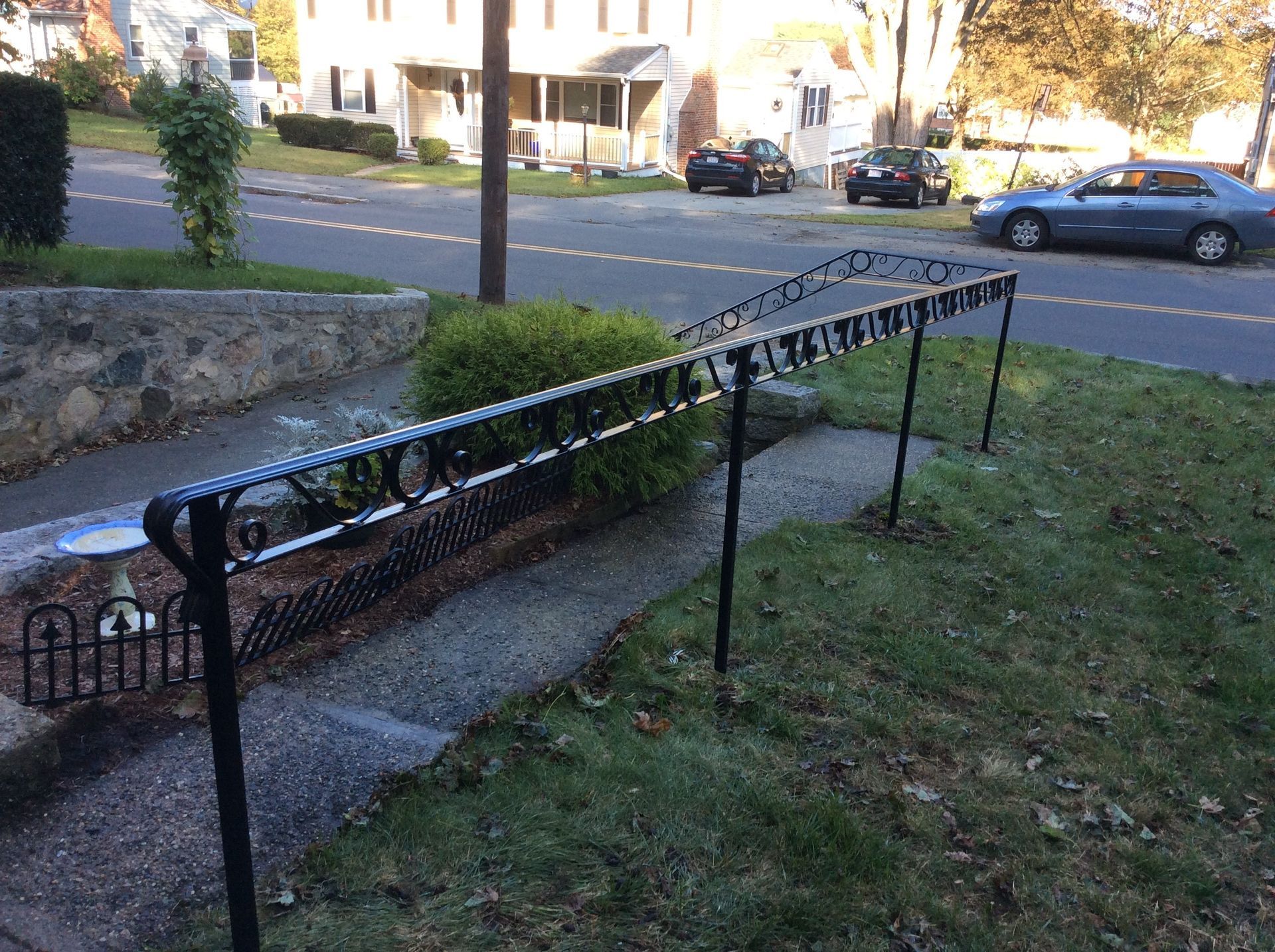 Black metal accessibility ramp with handrails beside a sidewalk and grassy lawn near a street.