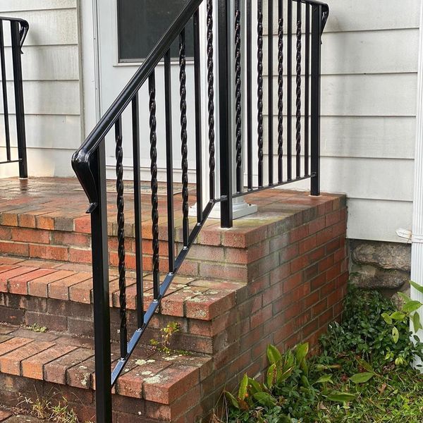 Black metal handrail with twisted balusters installed on brick steps leading to a white door.