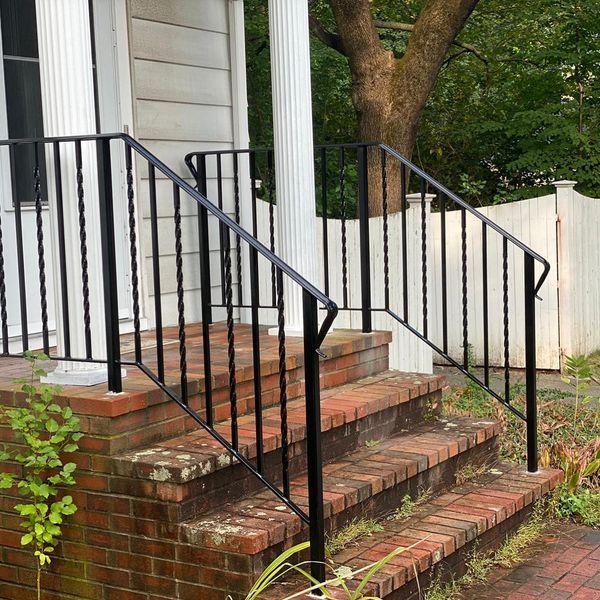 Black metal railings installed on brick front steps leading to a house entrance.