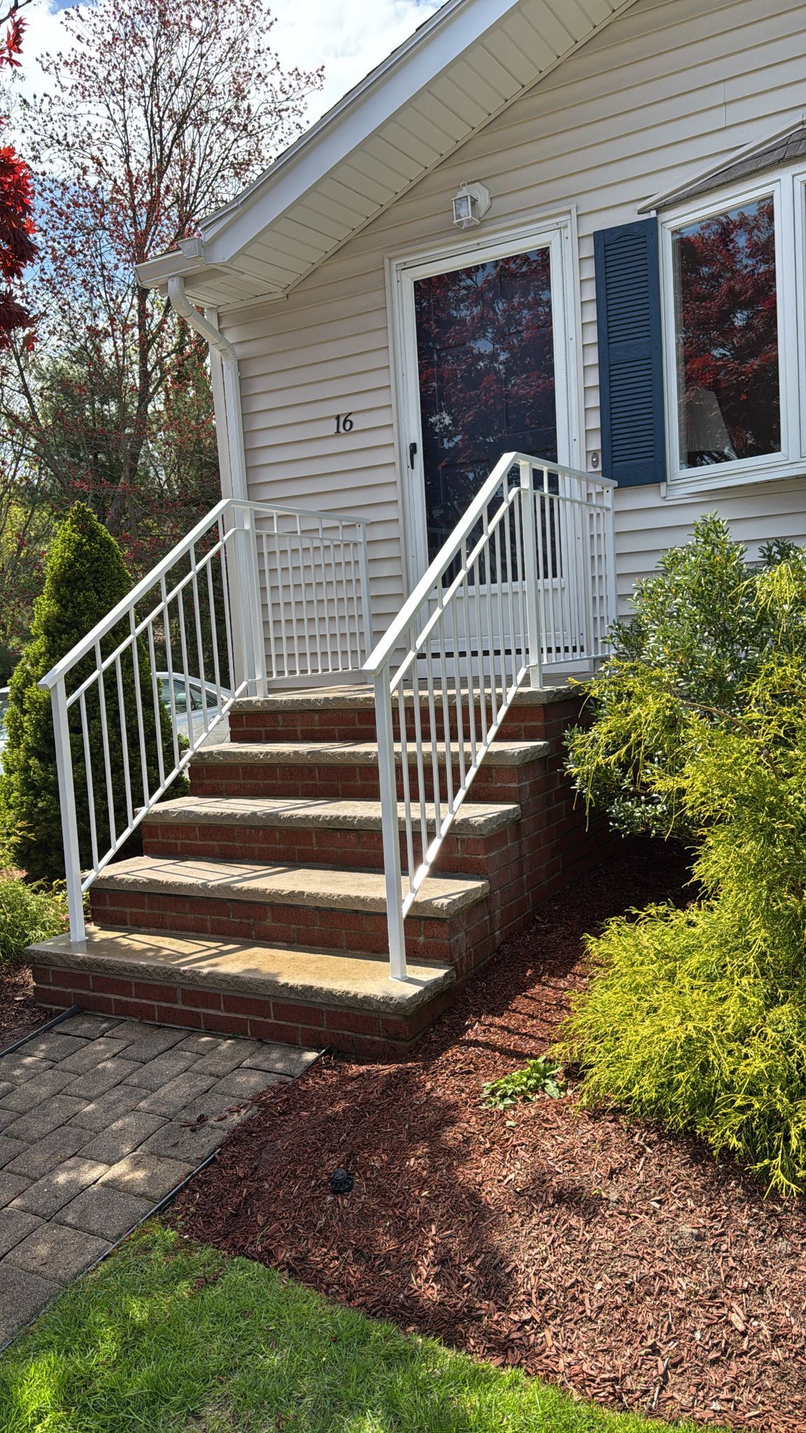Front steps of a house with white railings, brown stairs, and a blue door