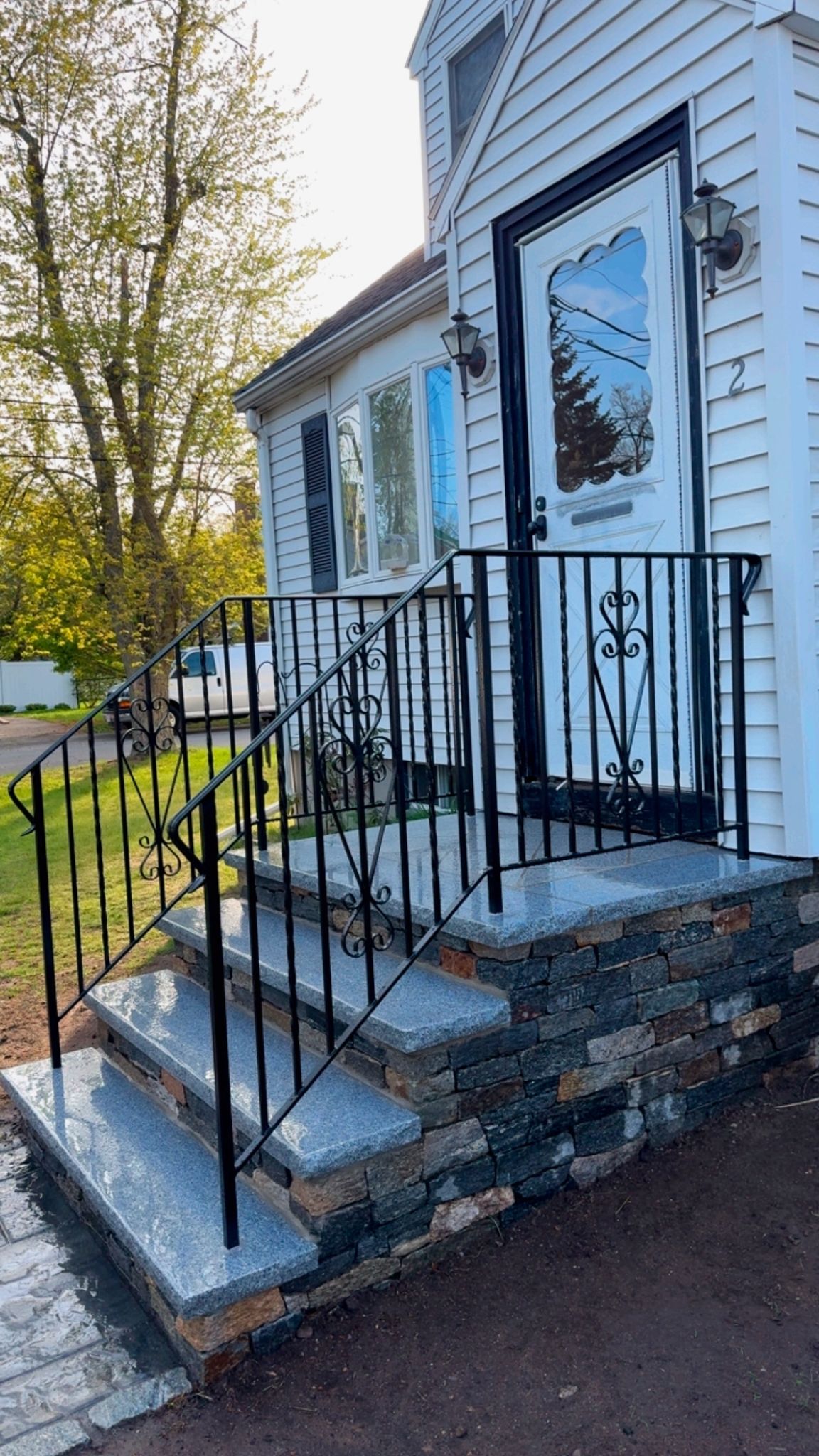 Front steps with black railings leading to a white house with a blue door and autumn trees nearby