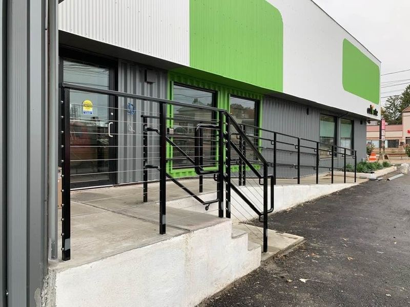Modern building entrance featuring a concrete ramp with black railings and a set of stairs leading to a glass door.