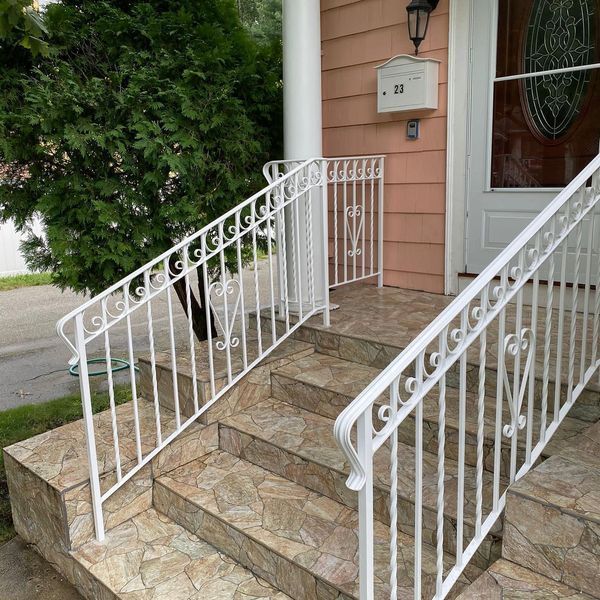 White wrought iron railings lead up tiled steps to the front entrance of a house with peach-colored siding.