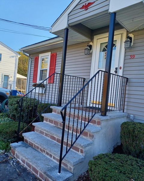 A small set of gray stone steps with black metal railings leading to the front door of a house with gray siding.