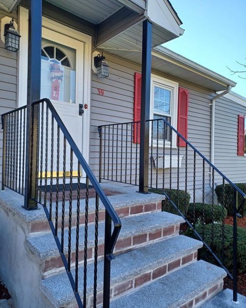 A front entrance with grey vinyl siding, red shutters, and granite steps featuring a black metal railing and porch supports.