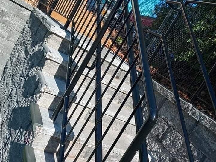 Outdoor stone stairs with black metal railings lead up a terraced landscape.