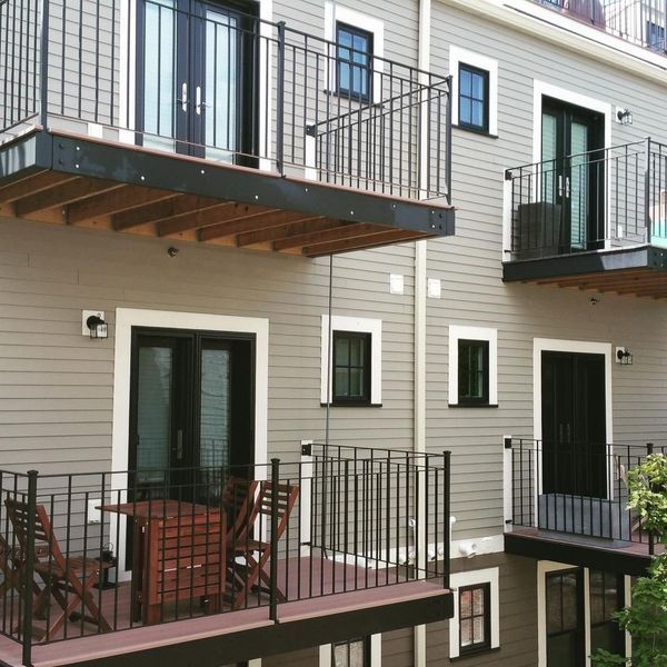 Light-gray building exterior with multiple levels of black metal balconies, sliding glass doors, and small square windows.