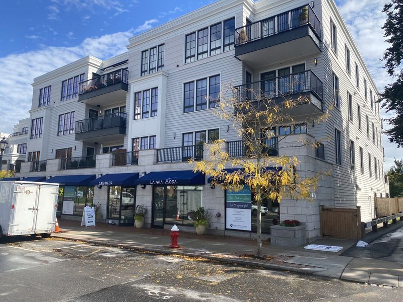 A light-colored multi-story apartment building with balconies and ground-floor storefronts under blue awnings.