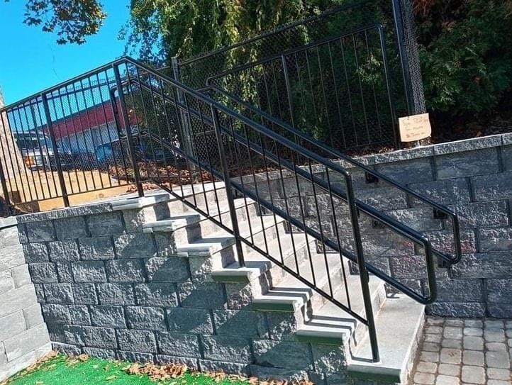 Concrete outdoor stairs with gray stone blocks and a black metal railing leading up to a platform.
