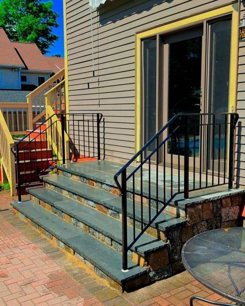 Stone stairs with black metal railings leading to a glass sliding door on a house exterior with a brick patio.