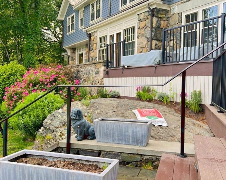 Black handrails lead up to a blue and stone-clad house with tiered landscaping, a concrete planter, and a dog statue.