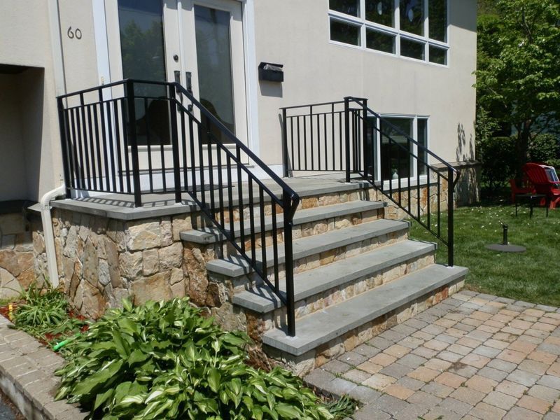 Stone steps with a black metal railing leading to a house entrance with double doors and a stone foundation.